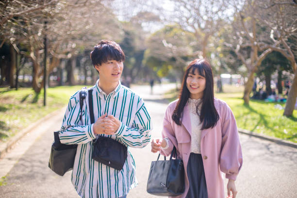 pareja joven caminando en parque público en un día soleado - cherry blossom spring day sakura fotografías e imágenes de stock