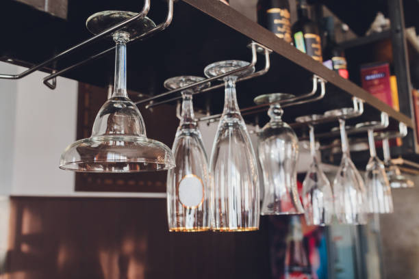 istock Closeup many upside down empty clear transparent crystal upturned wine glasses hanging in straight rows on brown wooden shelf, rack, showcase, stainless steel railing in bar, cabinet. 1214375305