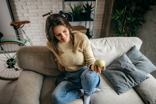 istock Young women sitting on sofa and eating apple 1214380508