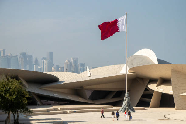 Qatar National Museum, Qatari Flag, and Doha Skyline Doha, Qatar - February 22, 2020: A sculpture and Qatari flag stand in front of the newly opened Qatar National Museum, with the modern skyline of downtown Doha in the distance. dhow photos stock pictures, royalty-free photos & images
