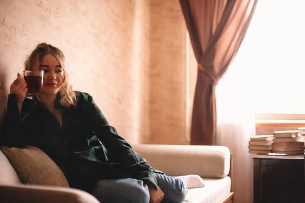 istock Young woman drinking tea while sitting on sofa at home 1214387112