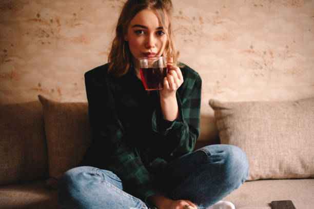 istock Young woman drinking tea while sitting on sofa 1214387115