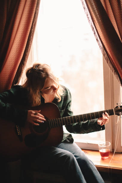 istock Young woman playing guitar at home 1214387181