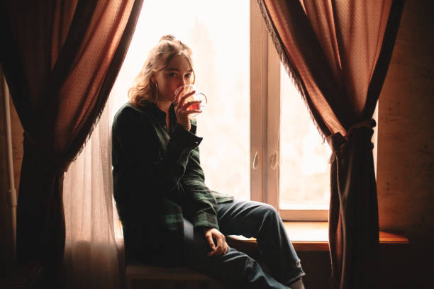 istock Young woman drinking tea sitting on windowsill at home 1214387298