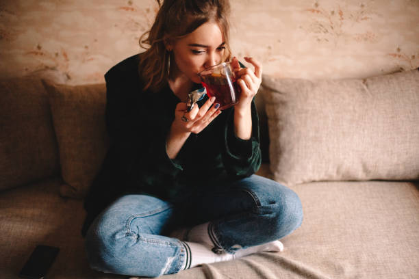 istock Young woman drinking tea while sitting on sofa at home 1214387314
