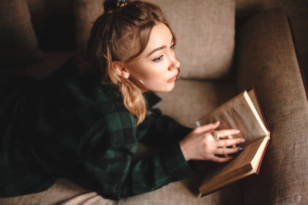 istock Young woman reading book at home 1214387367