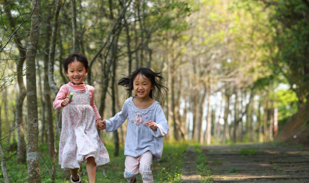 istock two Asian girls running and playing in a forest. 1214396849
