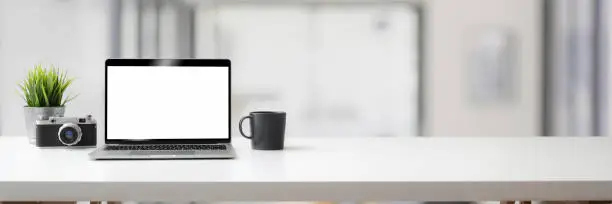 Cropped shot of minimal workspace with laptop, coffee cup, camera and copy space on white table with blurred background