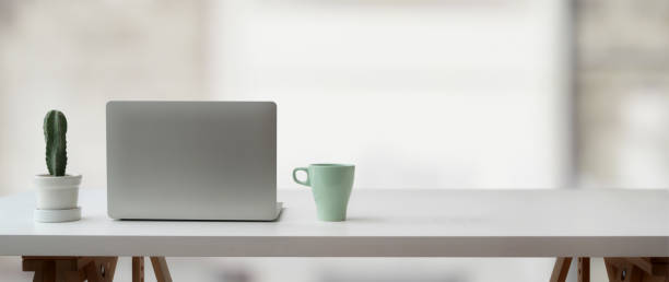 istock Cropped shot of simple workspace with laptop, cactus pot, mug and copy space on white table 1214397580