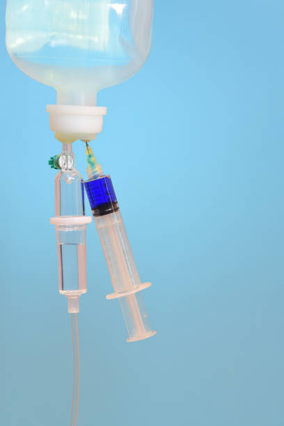 istock Close-up of an infusion system with an infusion containing a syringe containing blue liquid against a light blue background in medicine and space for vertical text 1214400787
