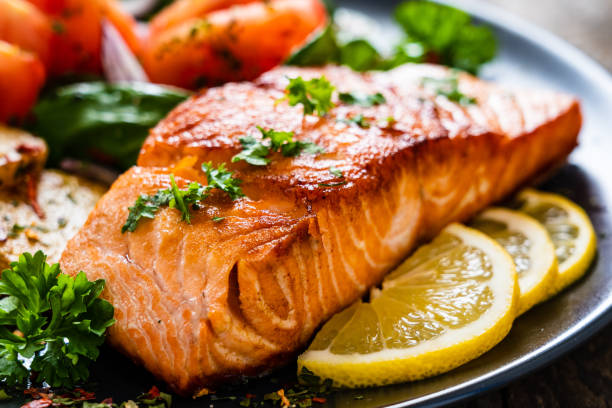 salmone alla brace, patate fritte e verdure su sfondo legnoso - salmone arrosto foto e immagini stock