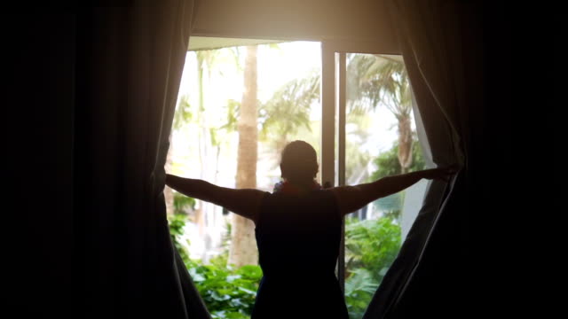 Woman exposing curtains and Looking at the tropical garden in slow motion 180fps
