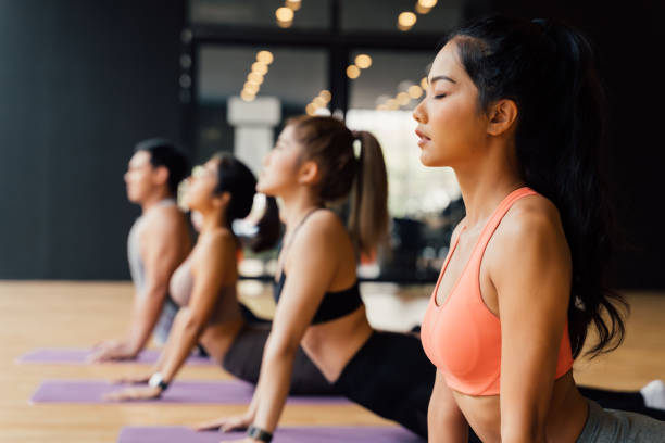 groupe de personnes asiatiques de forme physique faisant le yoga vers le haut le chien posent sur des nattes au studio de yoga. jeunes femmes et homme exerçant à gyn - muscular build wellbeing exercise equipment instructor photos et images de collection