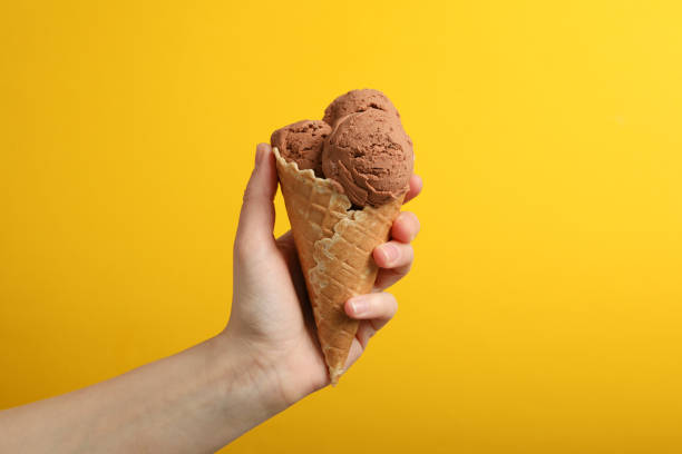 istock Female hand holds ice cream on yellow background, space for text 1214428156