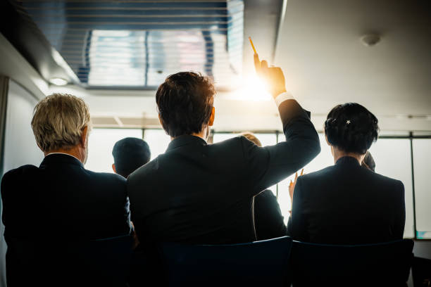 ビジネスマンが会議室で会議のリーダーとの意見のトレーニングで話している間、ビジネスオーディエンスは手を挙げる - hand raised asking women businesswoman ストックフォトと画像