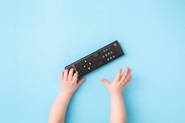 Infant hand reaching after remote control on light blue table background. Pastel color. Closeup. Favourite baby thing. Top down view.