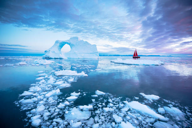 barco de vela rojo que navega entre hielobergs en groenlandia. - sol de medianoche fotografías e imágenes de stock