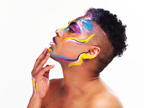 Cropped shot of a gender fluid young man wearing face paint against a white background