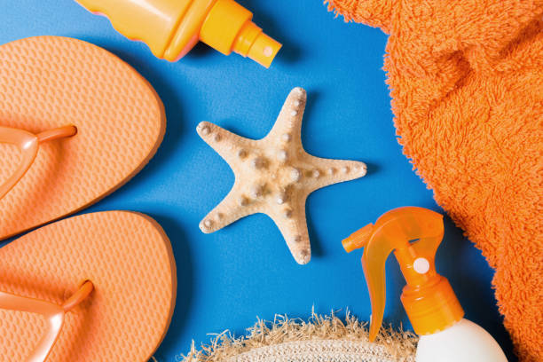 istock Summer beach flat lay accessories. Sunscreen bottle cream, straw hat, flip flops, towel and seashells on colored Background. Travel holiday concept with copy space 1214446118