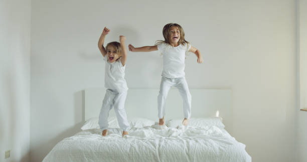 istock Two sisters, wearing white pajamas, fight with pillows and have fun. 1214448225