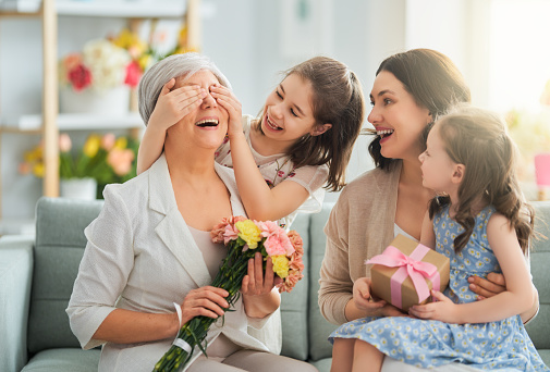 Happy mother's day! Children daughters are congratulating mom and granny giving them flowers and gift. Grandma, mum and girls smiling and hugging. Family holiday and togetherness.