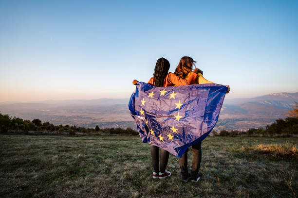 Two multi-ethnic women holding European Union flag Two young pretty multi-ethnic women holding European Union flag on meadow. Unity stock pictures, royalty-free photos & images