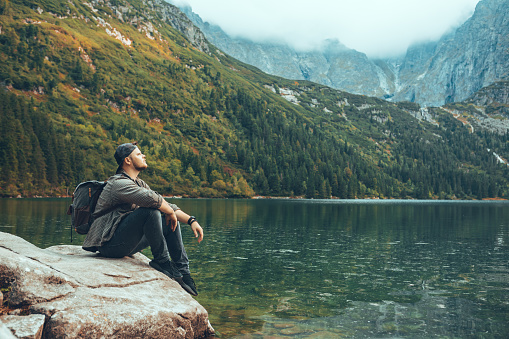 man sitting on the rock in front of lake in mountains enjoying the view hiking concept