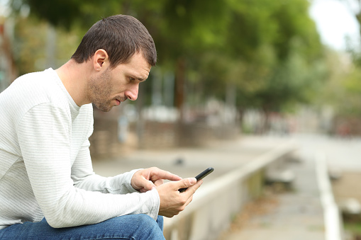 Side view of serious adult man using smart phone alone in a park