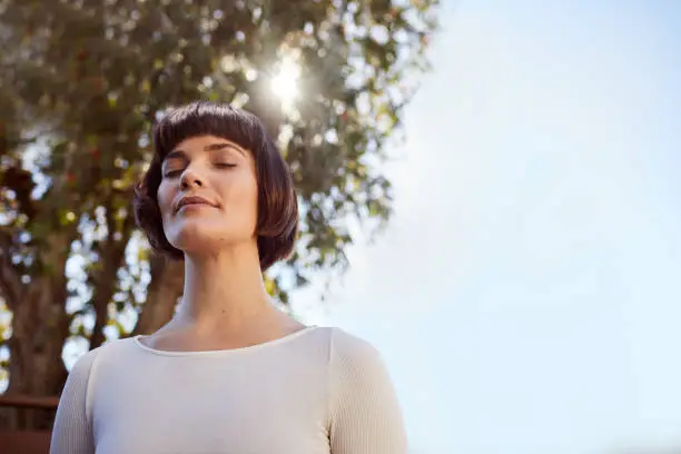 Photo of Young woman standing outside and meditating with her eyes closed