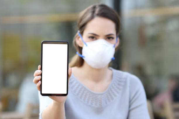 istock Woman with mask showing phone with blank screen 1214455561