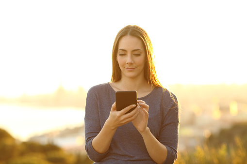 Front view portrait of a serious woman using smart phone on the outskirts at sunset