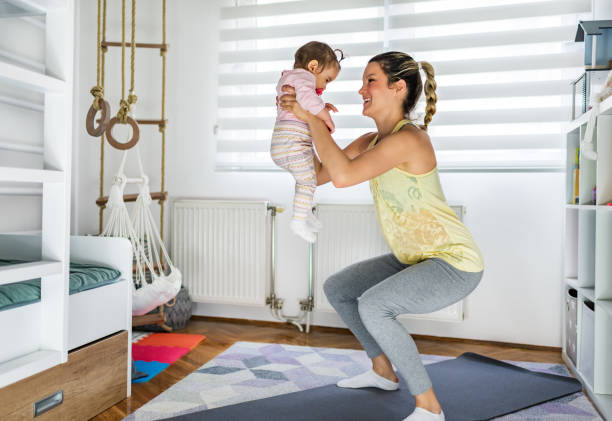 Mother exercise with her baby at home Shot of an attractive young woman with her baby girl while doing exercise. Woman working squats while holding her baby. baby squatting stock pictures, royalty-free photos & images