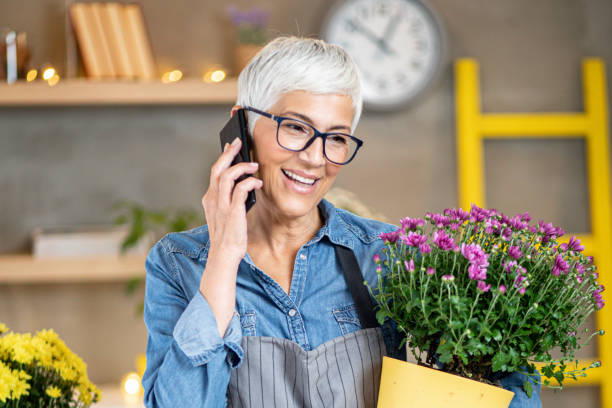 florista de mujer madura usando tecnología moderna. - planting clothing gray hair human age fotografías e imágenes de stock