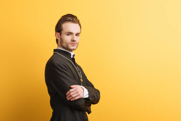 istock confident catholic priest with crossed arms looking at camera isolated on yellow 1214461898