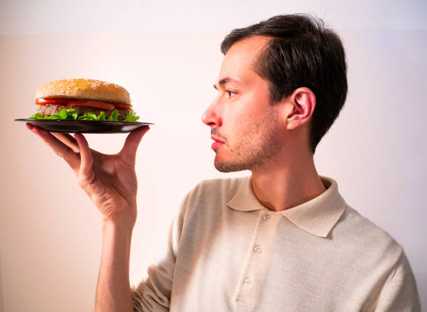 istock Handsome young man holding, looking and examining tasty hamburger for hexamination 1214462453