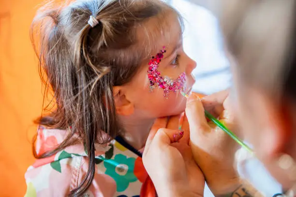 A young girl getting glitter painted on her face by an unrecognizable face painter. She is at a food festival in Whitley Bay.