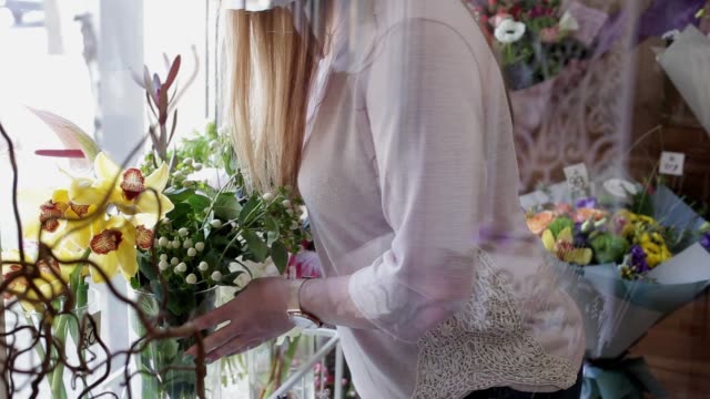 Girl florist arranges flowers and selects three beautiful fresh yellow orchids for a bouquet near a window in a flower shop.