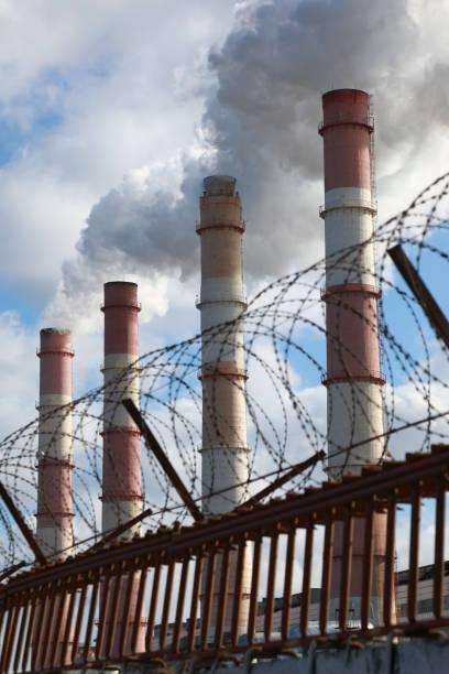 istock Factory chimneys smoke behind a fence with barbed wire 1214463608