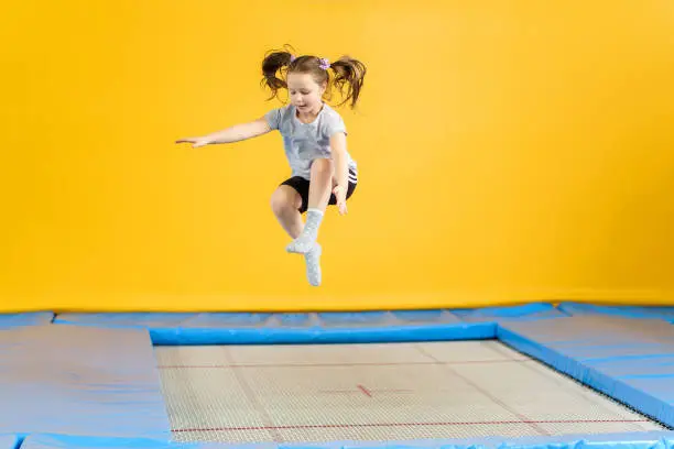 Happy child girl jumping on trampoline in fitness center