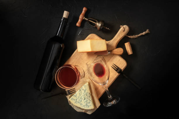istock Wine and cheese tasting, overhead shot on a black background, with a cork, corkscrew, and a bottle 1214465618