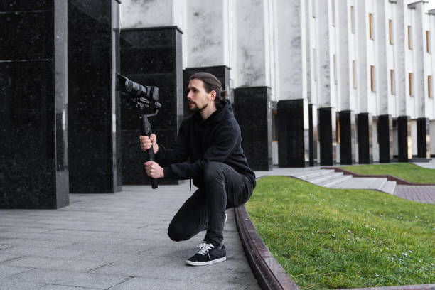 istock Young Professional videographer holding professional camera on 3-axis gimbal stabilizer. Pro equipment helps to make high quality video without shaking. Cameraman wearing black hoodie making a videos. 1214465678