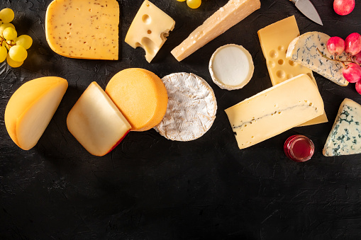 Many different types of cheese, shot from the top on a black background with a place for text