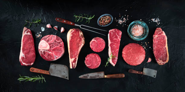 diverses coupes de viande, tirées du haut sur un fond noir avec des condiments et des couteaux, un panorama plat laïc - veal rosemary meat steak photos et images de collection