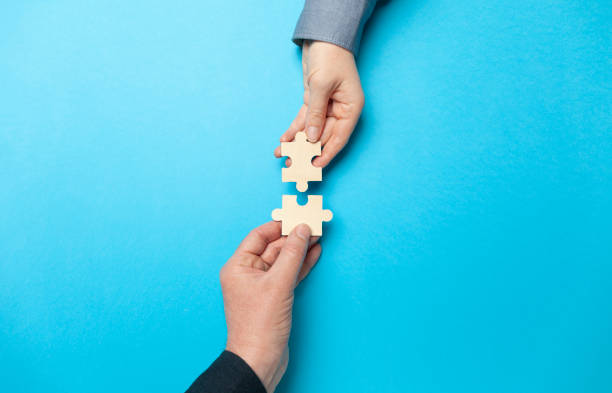 istock Two hands connect puzzles on a blue background. Cooperation and teamwork in business. Collaboration people for success 1214468227