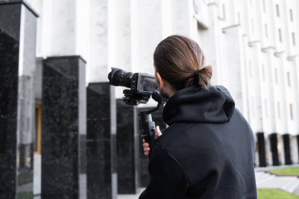 istock Young Professional videographer holding professional camera on 3-axis gimbal stabilizer. Pro equipment helps to make high quality video without shaking. Cameraman wearing black hoodie making a videos. 1214469292