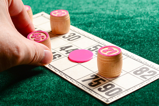 Lotto, classic family board game. Close up view of fingers of a man putting wooden barrel on card. Vintage game, bingo.