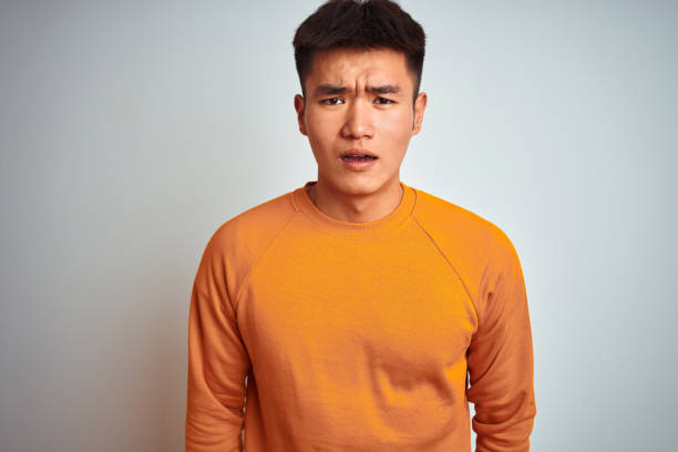 istock Young asian chinese man wearing orange sweater standing over isolated white background afraid and shocked with surprise expression, fear and excited face. 1214472152