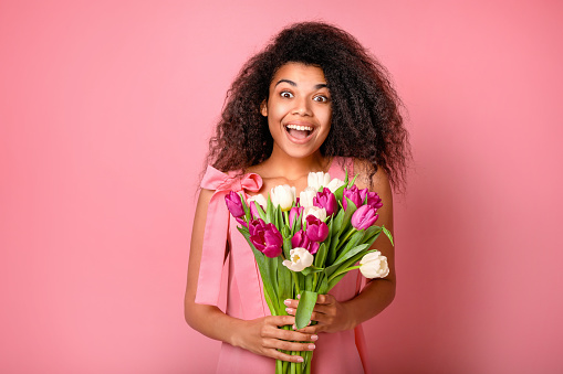 Young african woman with flowers on pink background. Women's day concept