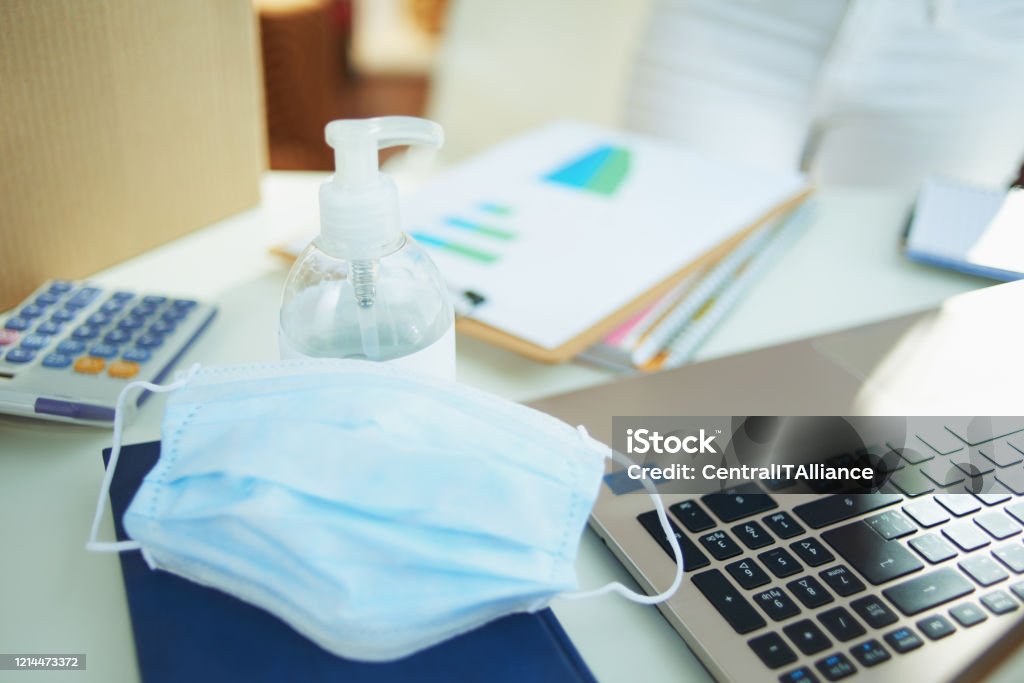 medical mask and hand disinfectant on table in home office Closeup on medical mask and hand disinfectant on the table in temporary home office during the coronavirus epidemic in the living room in sunny day. Coronavirus Stock Photo