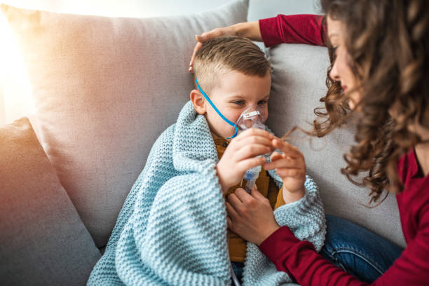 junge frau mit sohn beim einatmen mit einem vernebler. - asthmatic child asthma inhaler inhaling stock-fotos und bilder